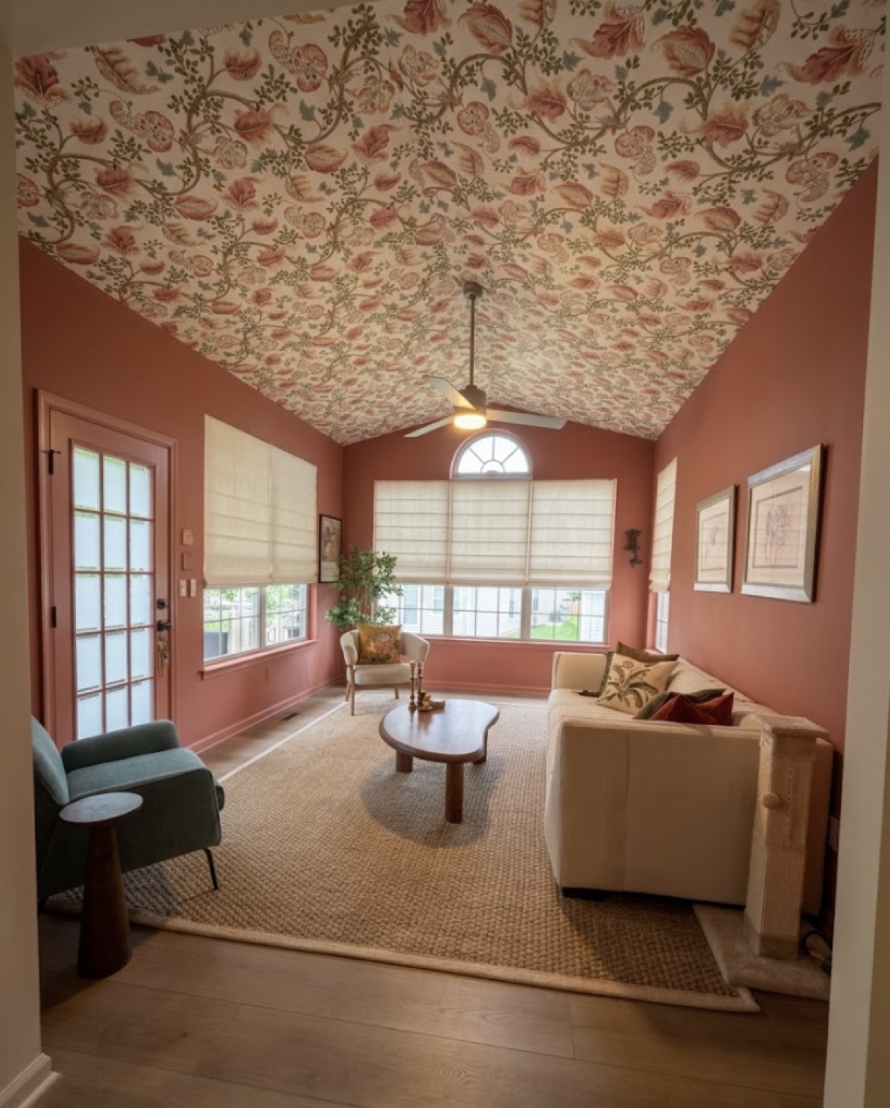 The finished sunroom with patterned wallpaper ceiling, coral walls, and new furniture